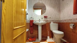 A bathroom with a wooden door, a round mirror, a sink, a toilet, and a red towel hanging on the wall. - Avenue viewpoint (Albaida)