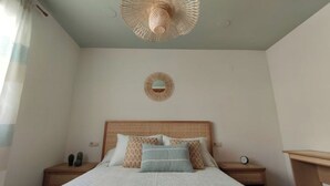 A bedroom with a bed, a round mirror on the wall, and a woven ceiling light fixture. - Avenue viewpoint (Albaida)