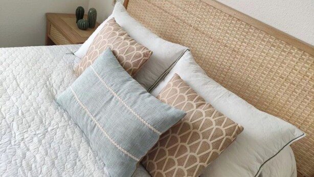 A neatly made bed with a patterned quilt and several pillows, including a light blue one with a decorative border. - Avenue viewpoint (Albaida)