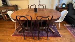 Une table de salle à manger ronde en bois, entourée de six chaises, avec une machine à café et un meuble en arrière-plan.