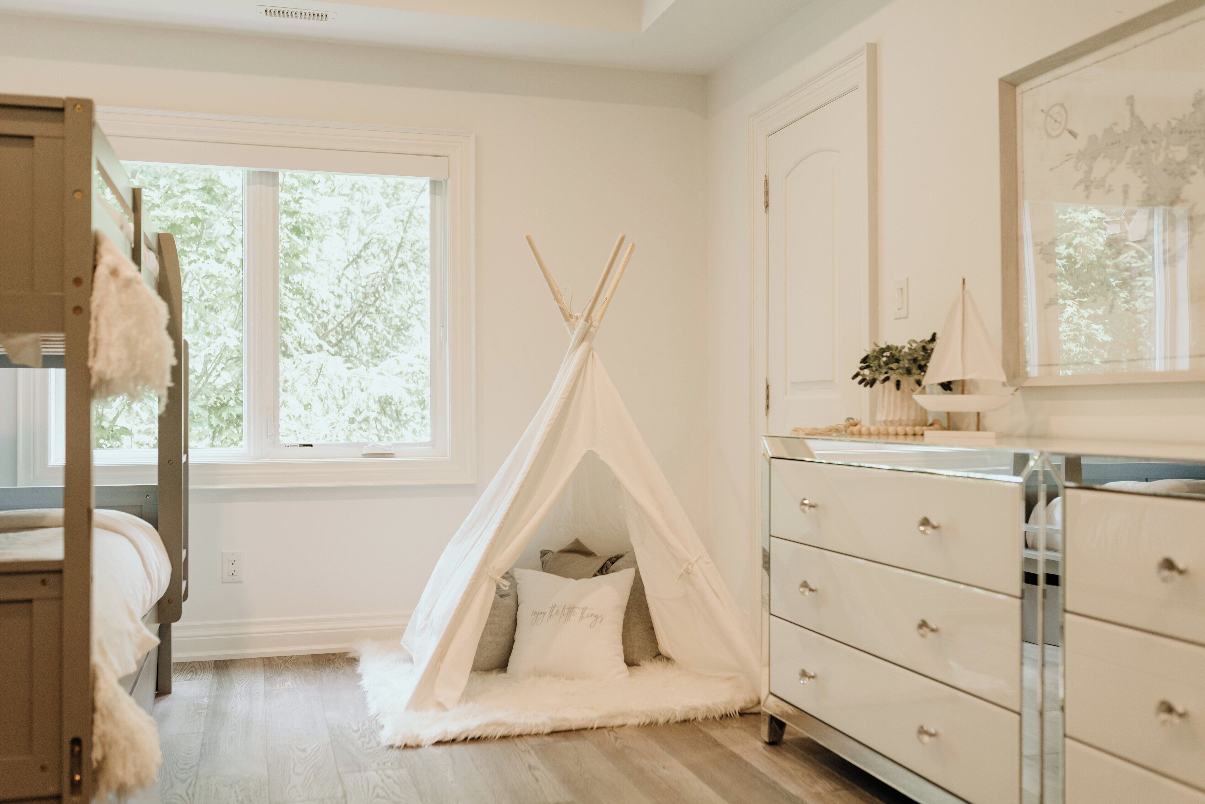 A bedroom with a white bed, a white dresser, a window, and a teepee tent.