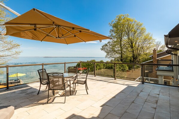 A terrace with a table and chairs, a large umbrella, and a view of the water.