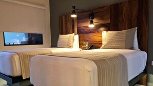 Une chambre d’hôtel moderne avec deux lits, une tête de lit en bois, des lampes de chevet et une petite table sur laquelle se trouvent un téléphone et une plante.