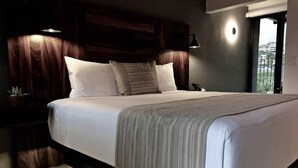 A modern bedroom with a large bed, dark wood headboard, and a view of the outdoors.