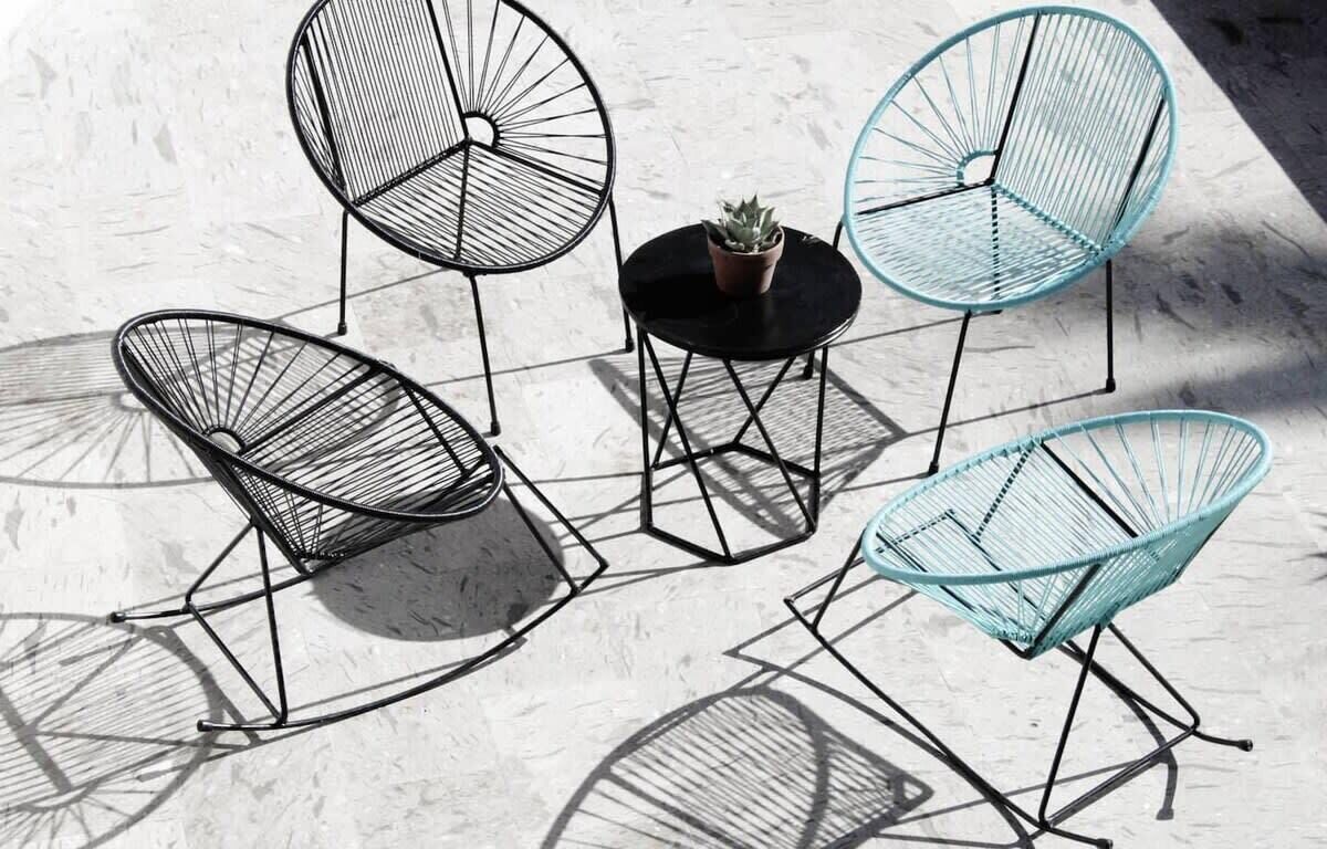 A set of four wireframe chairs with a small table and a potted plant, arranged on a concrete floor.