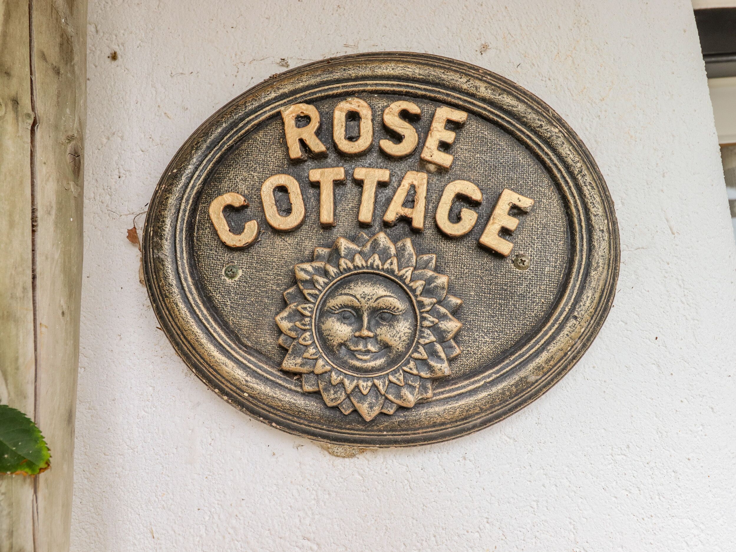 A metal plaque with the inscription "ROSE COTTAGE" and a sun design.