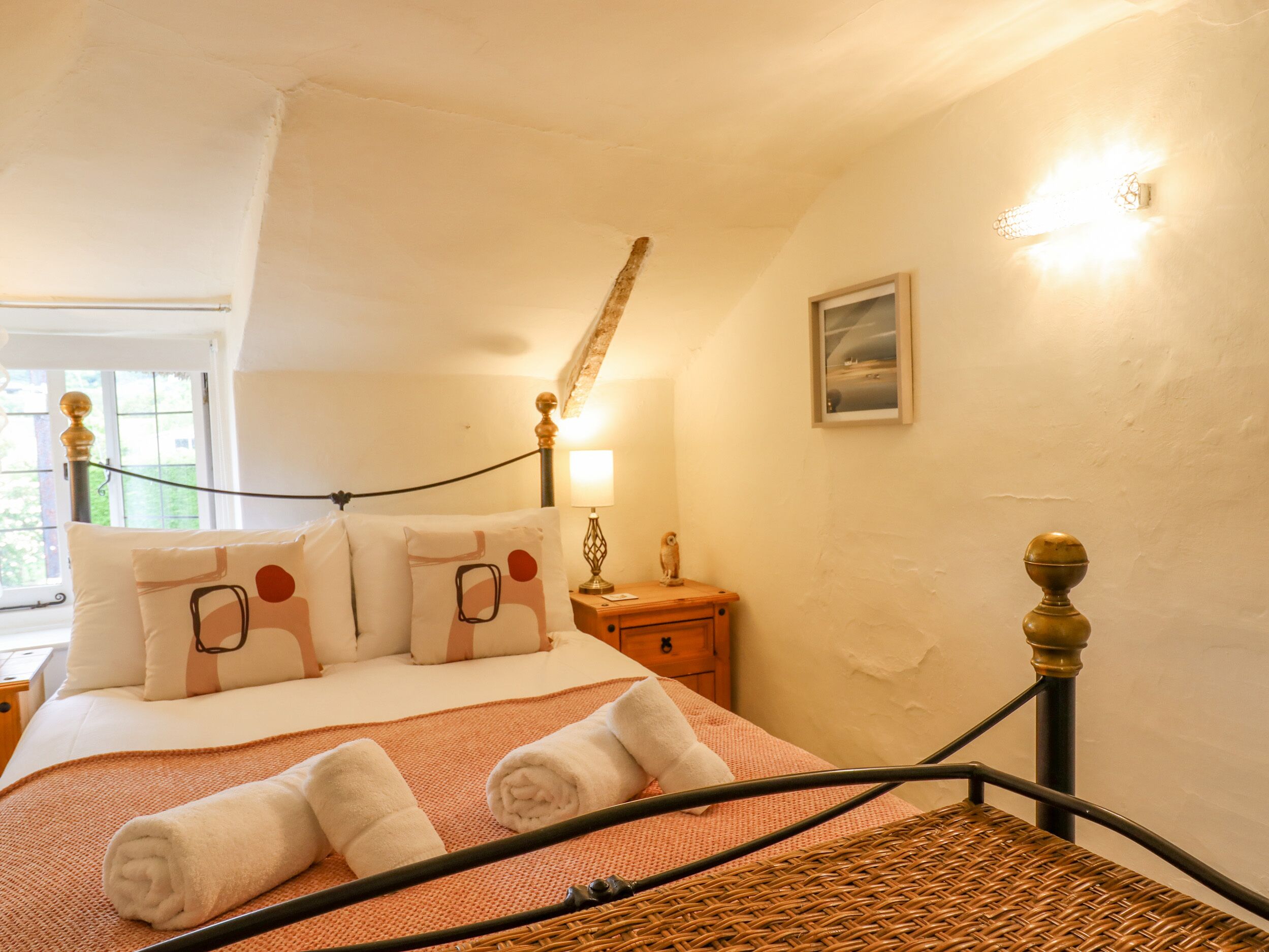 Um quarto aconchegante com uma cama, mesa de cabeceira, abajur e um quadro na parede.