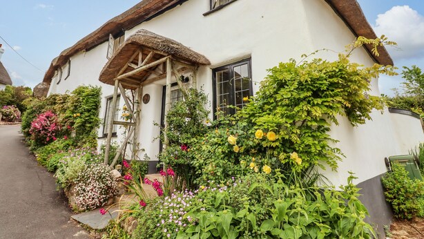 Una casa tradicional con techo de paja y un jardín lleno de flores y plantas.