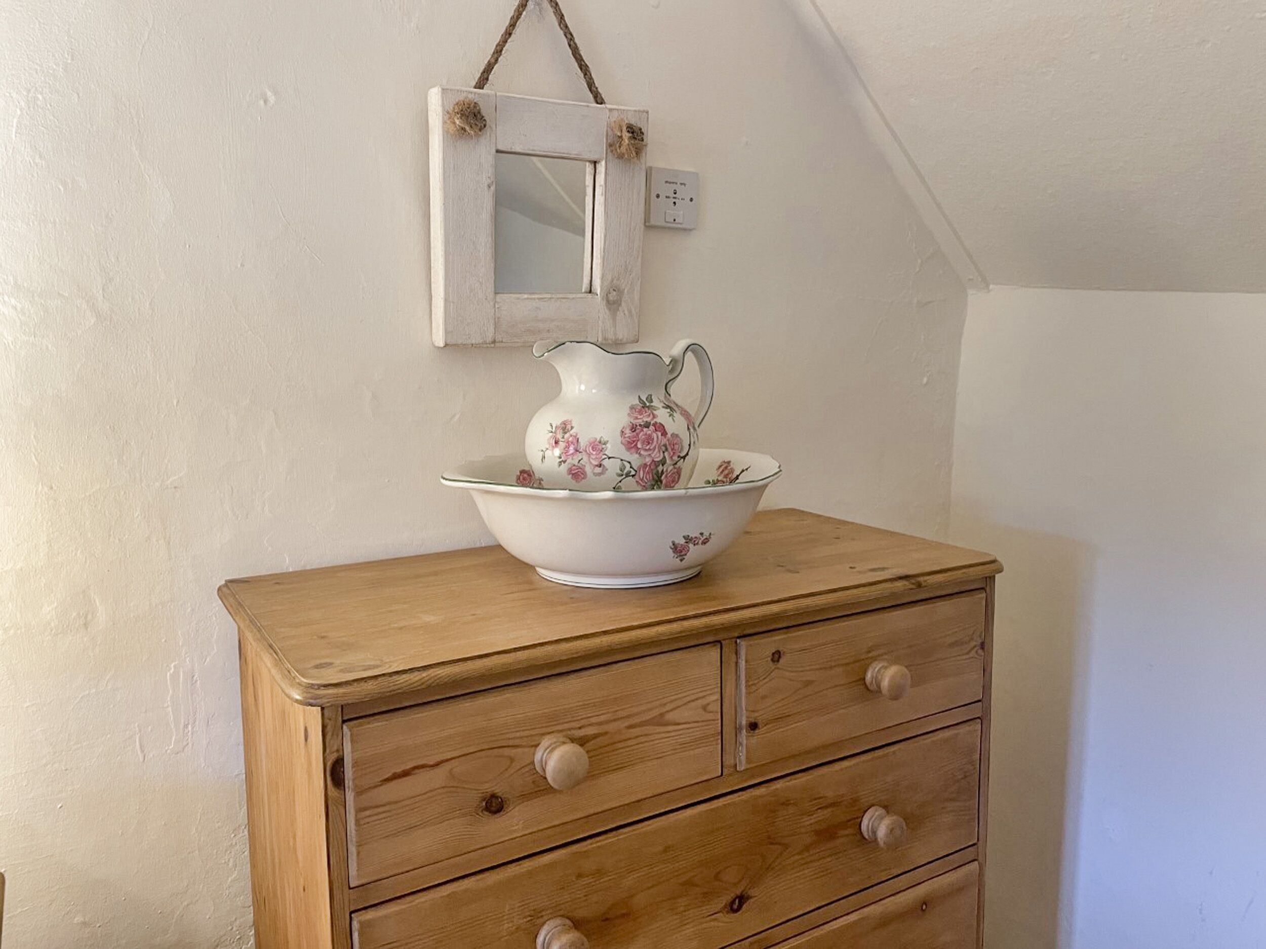 A wooden dresser with three drawers and a white ceramic jug with floral patterns on top.