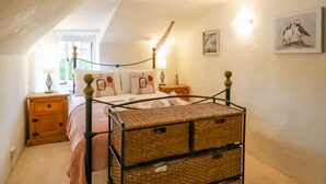 Un dormitorio acogedor con una cama con dosel, mesitas de noche de madera, un aparador de mimbre y una ventana con cortinas.
