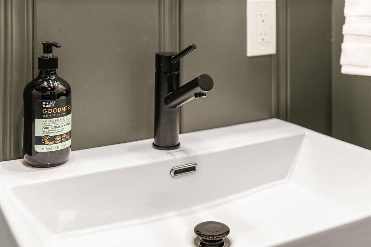 A bathroom sink with a black faucet and a bottle of hand wash soap.