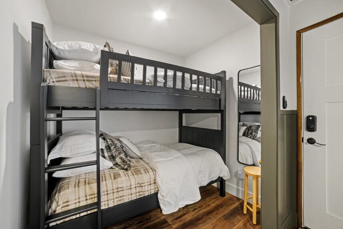 A bunk bed room with a wooden floor, a desk, and a mirror.