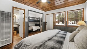 A bedroom with a bunk bed, a large bed, wooden ceiling, and a window with blinds.