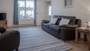 Una sala de estar con un sofá de cuero, un televisor, una mesita con una radio y una alfombra estampada.