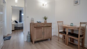 Una habitación moderna y luminosa con un armario de madera, dos sillas, una mesita y una cama al fondo.