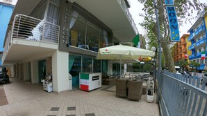 Exterior de un hotel con terraza, mobiliario exterior y un puesto de Heineken.
