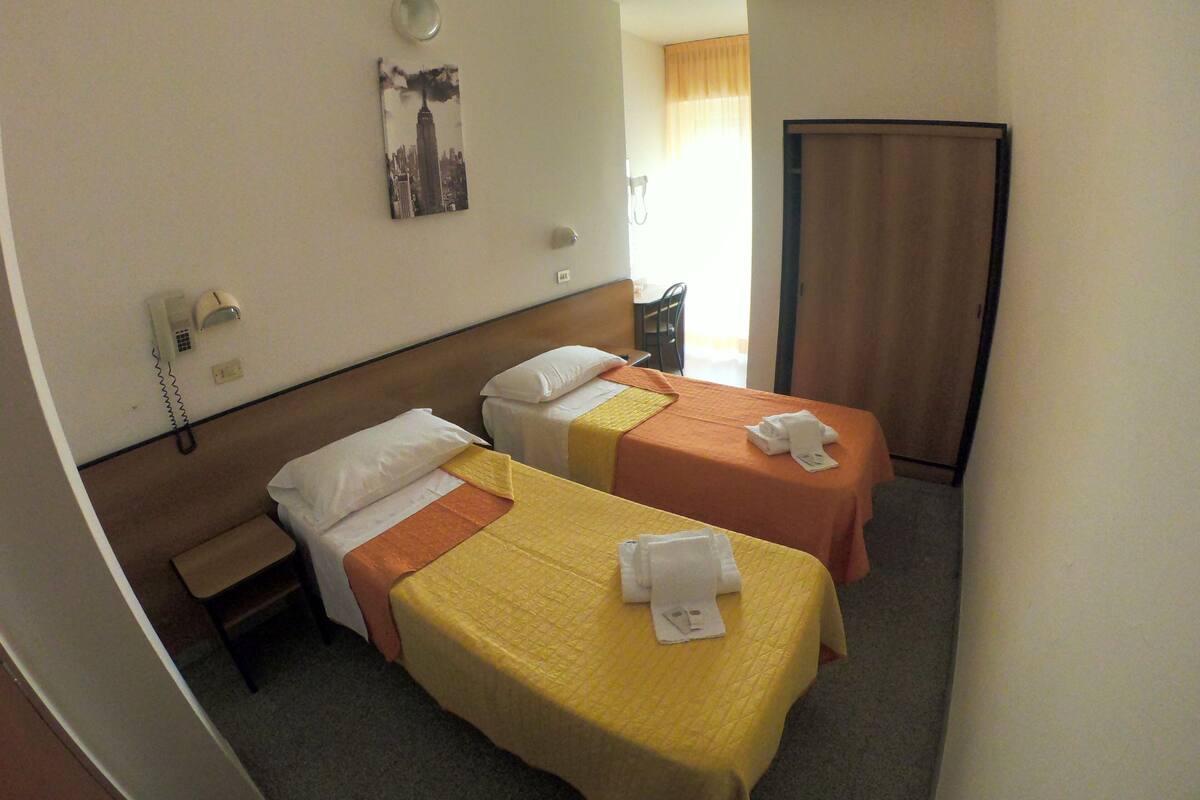 A hotel room with two single beds, a bedside table, a telephone, and a painting on the wall.
