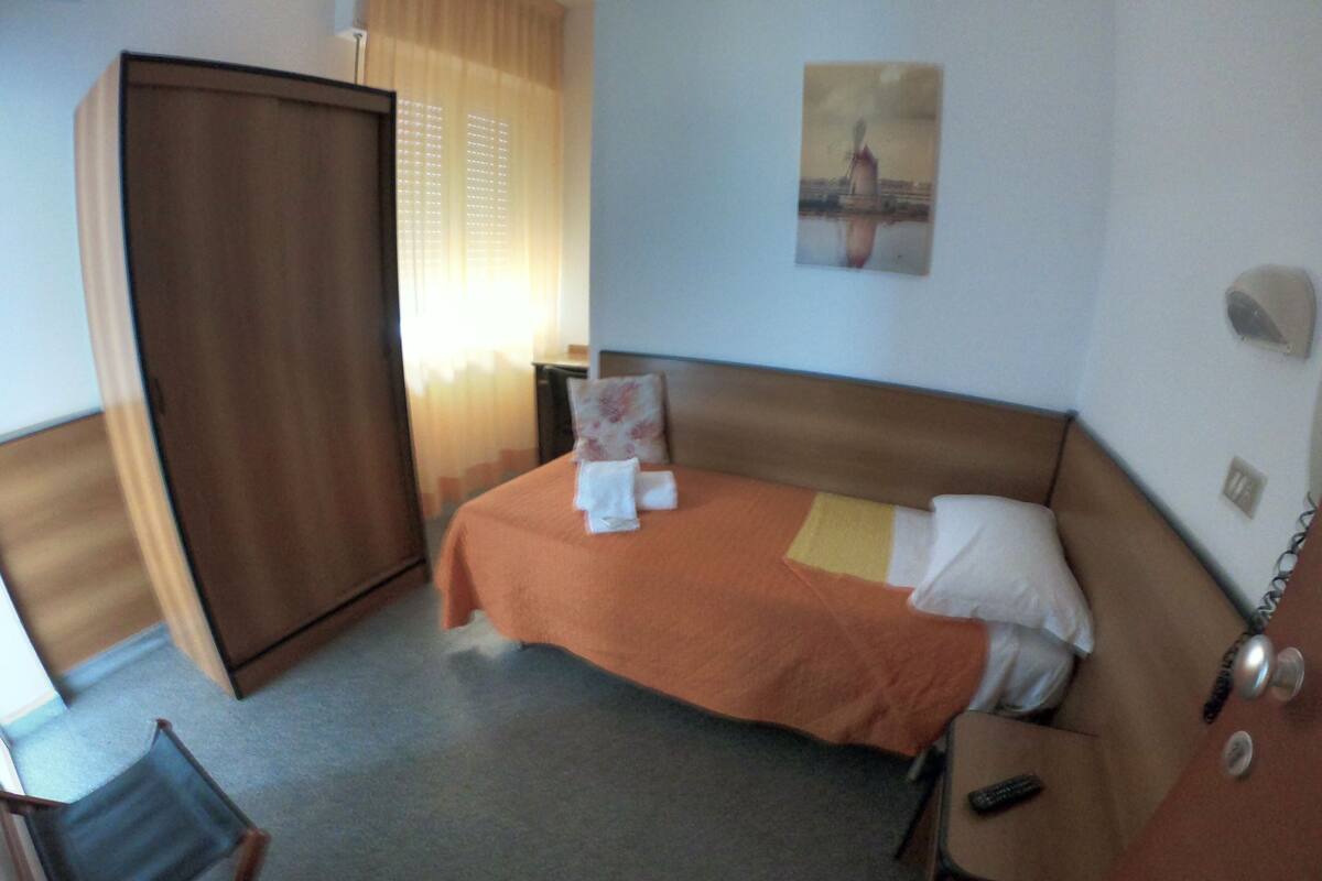 A hotel room with a bed, a wardrobe, a chair, and a painting on the wall.