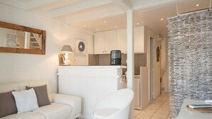 Un soggiorno moderno con un divano bianco, un tavolo rotondo bianco e una poltrona bianca. È presente anche una zona cucina con mobili bianchi e una macchina da caffè.