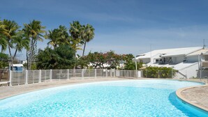 Una piscina con recinzione bianca, palme e un edificio con tetto bianco sullo sfondo.