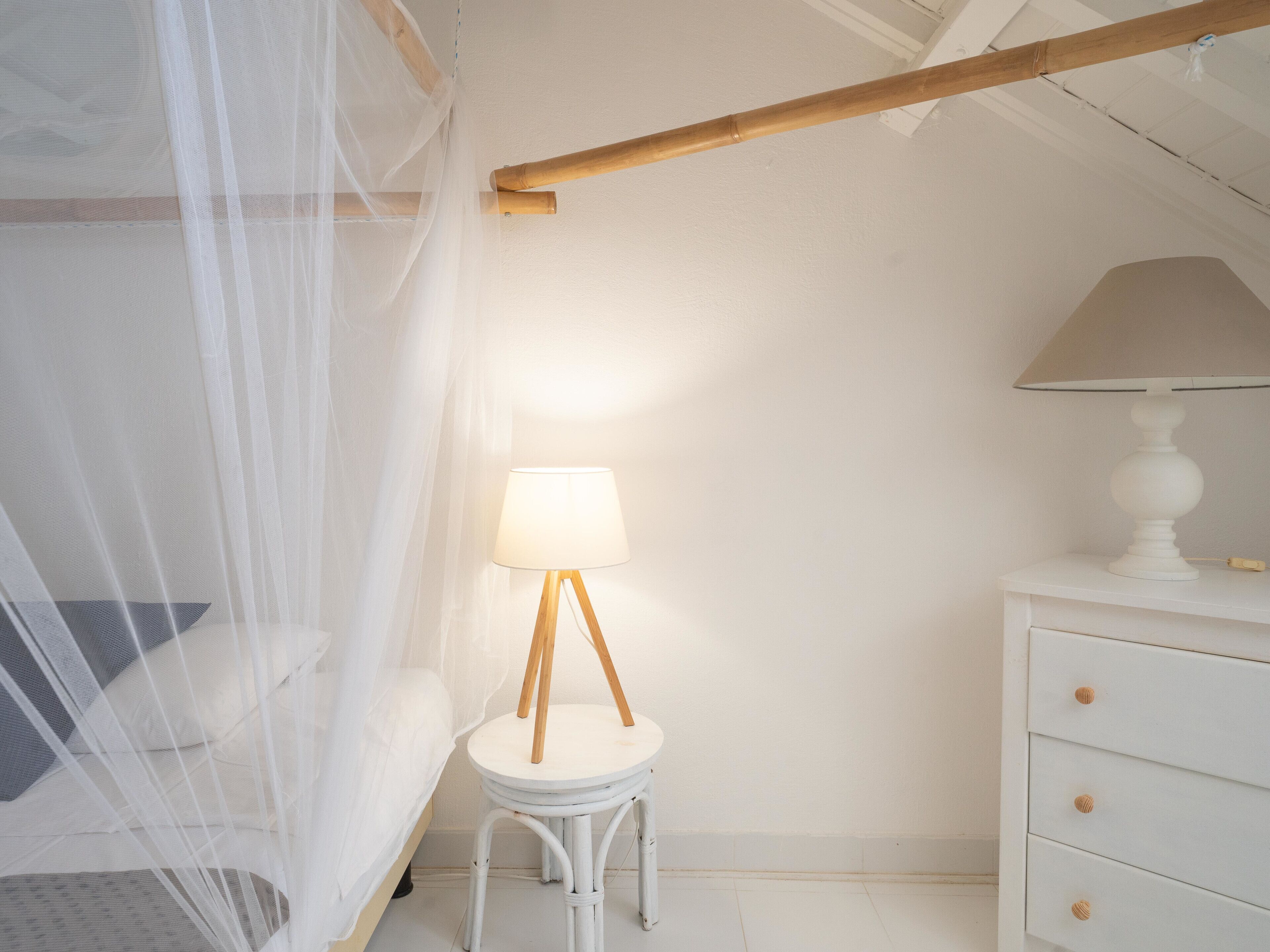 Un dormitorio con cama bajo un dosel, una mesita de noche con lámpara y un aparador con cajones.