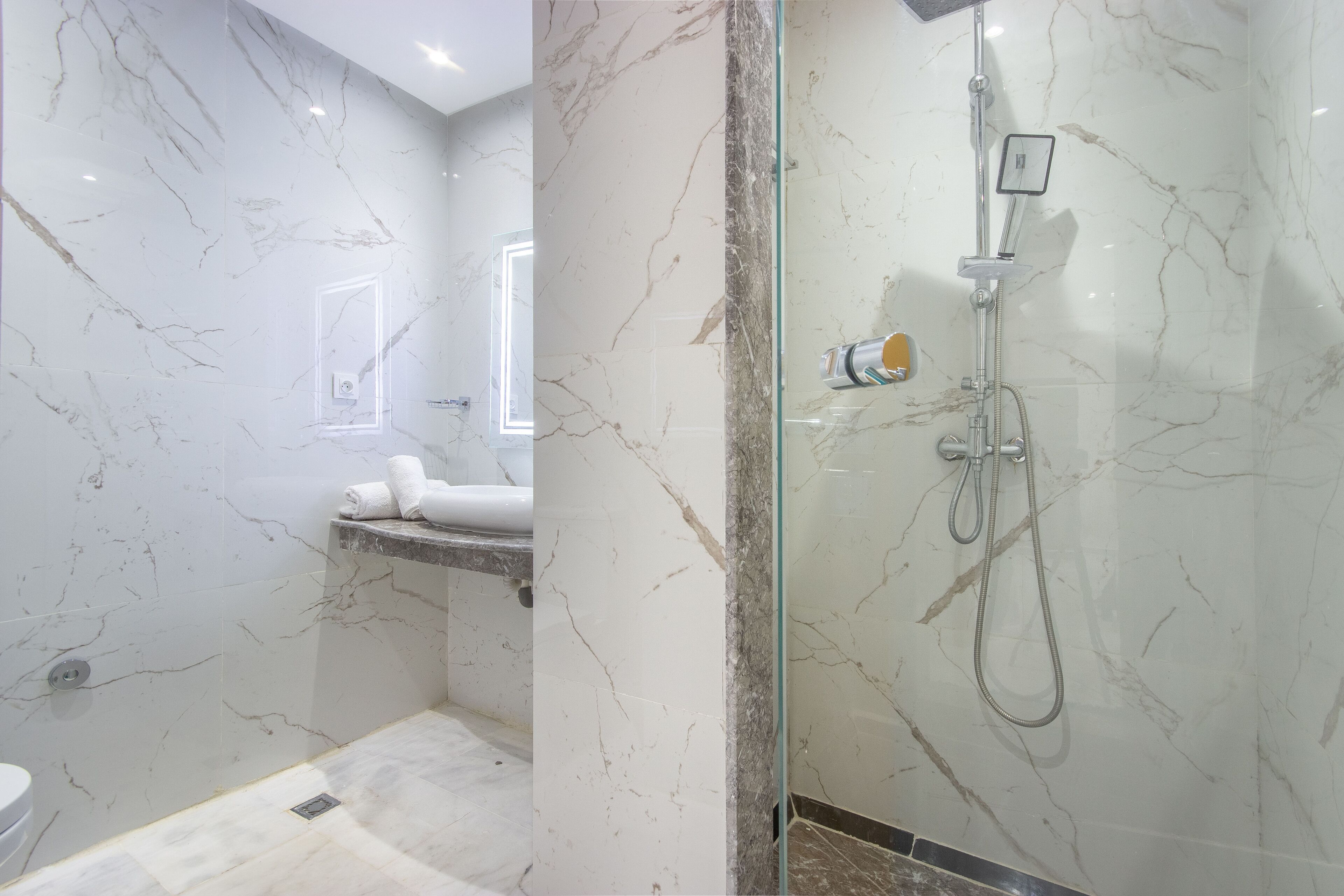A modern bathroom with marble walls, a glass-enclosed shower, and a visible toilet.