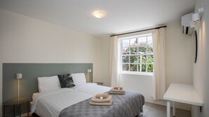 A bedroom with a bed, bedside tables, a window with curtains, and a wall-mounted air conditioner. - Apartment in the gated compound Jan Sofat near Jan Thiel Beach (Willemstad)