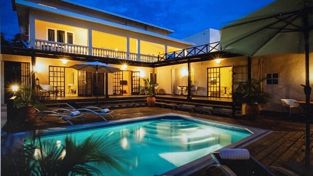 A pool area with lounge chairs and umbrellas, a covered patio, and a building with a balcony. - Apartment in the gated compound Jan Sofat near Jan Thiel Beach (Willemstad)