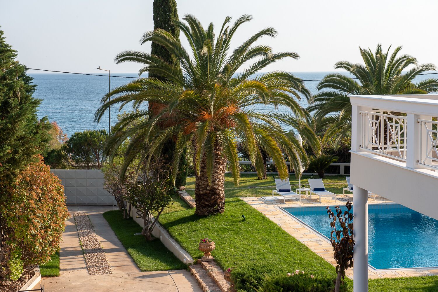 Ein Poolbereich mit Palmen, freier Blick auf das Meer und ein weißes Gebäude mit Balkon.