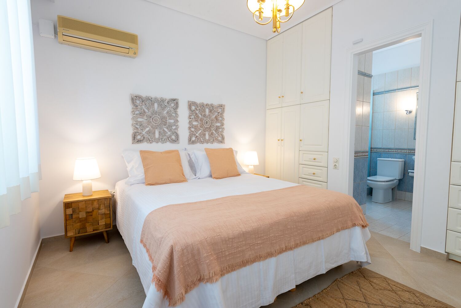 Ein Schlafzimmer mit Bett, Nachttischlampen, einem Kleiderschrank und einem durch eine offene Tür einsehbaren Badezimmer.