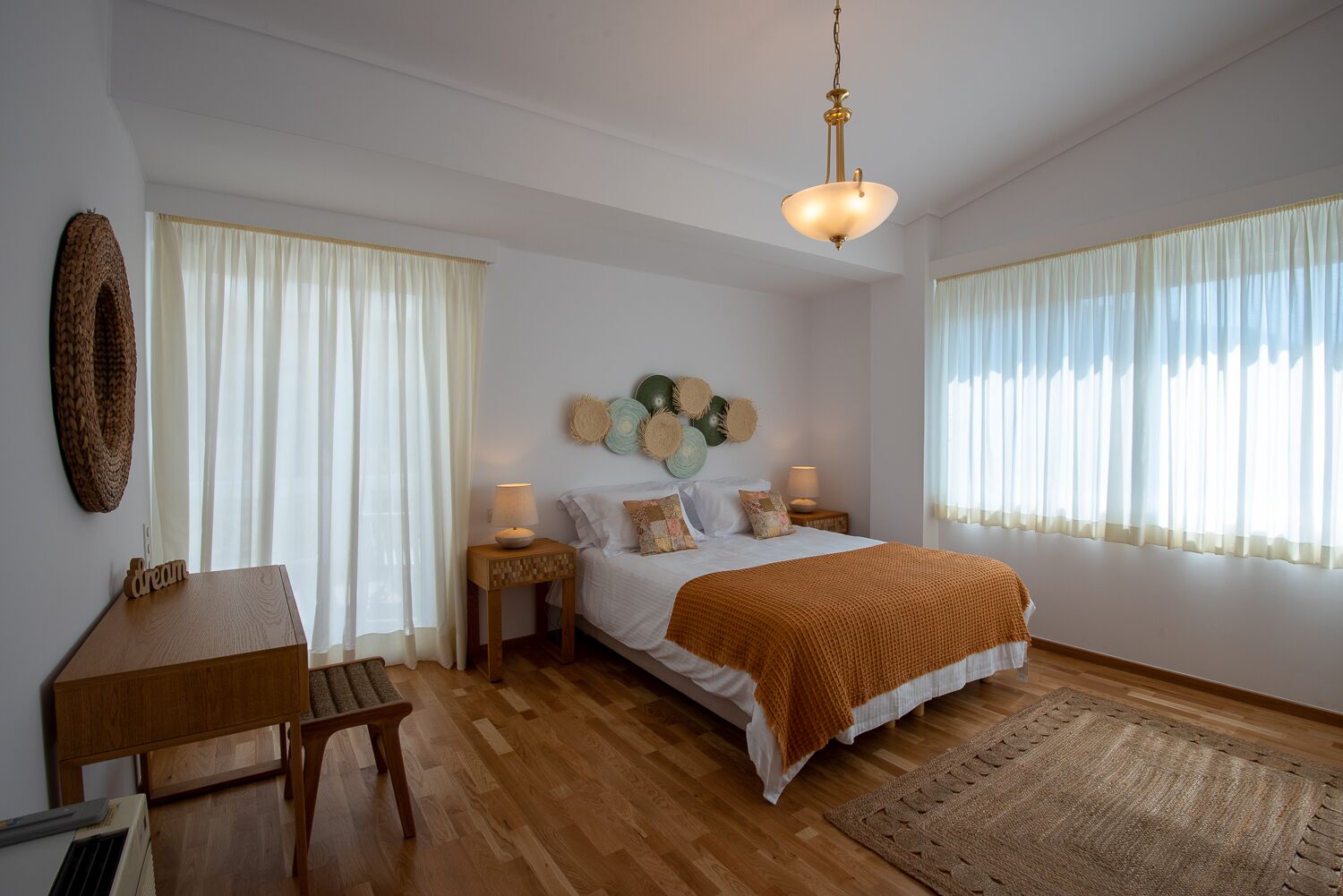 A bedroom with a wooden bed, bedside tables, a desk, and a hanging light fixture.