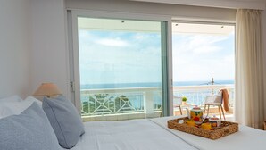 Una camera d'albergo con un letto, una lampada, un vassoio con articoli per la colazione e un balcone vista mare.