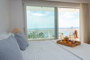 Habitación de hotel con cama, lámpara, bandeja con alimentos para el desayuno y balcón con vista al mar.