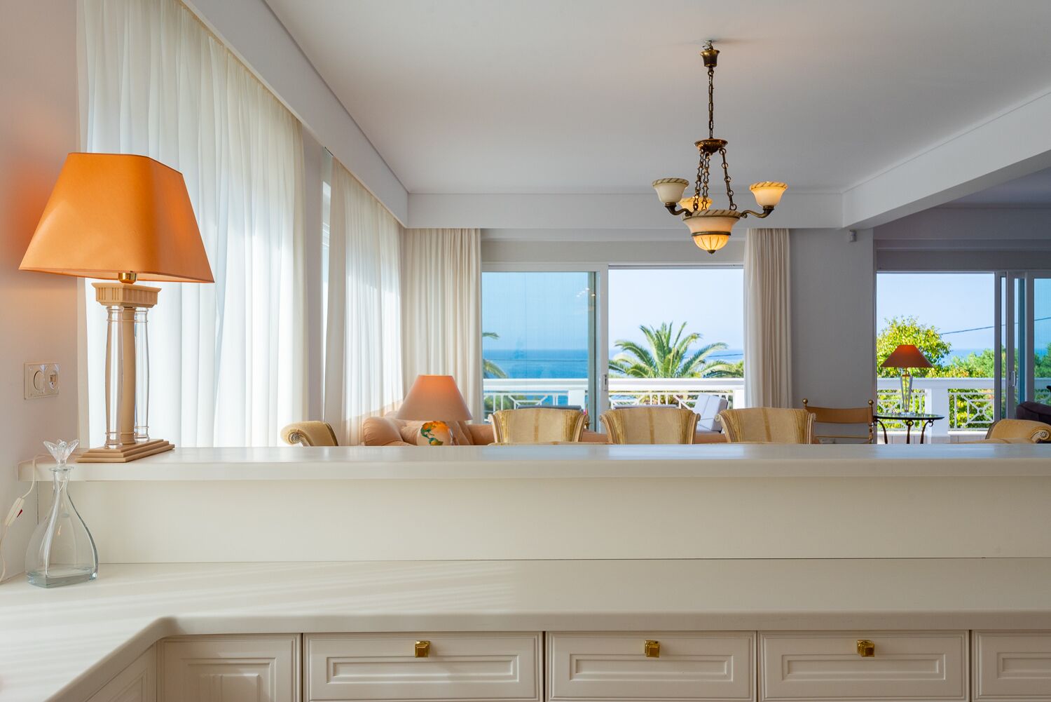 A hotel room with a large window, a chandelier, and a white console table with lamps.