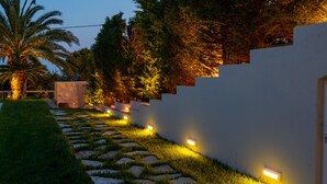Un sentiero con pietre a formare un percorso conduce a un muro bianco con faretti incassati.