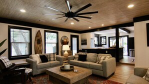 A spacious living room with a ceiling fan, large windows, and a cozy seating area with sofas and a coffee table.