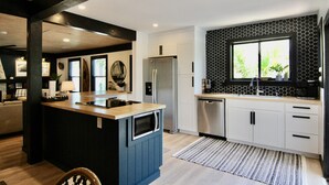 A modern kitchen with a central island, stainless steel appliances, and a black and white tiled backsplash.
