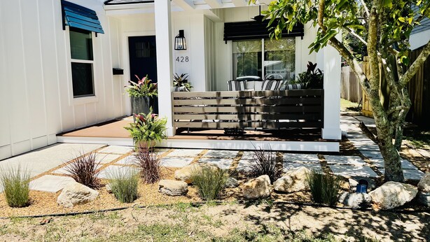A modern house with a covered patio, a number 428 sign, and a stone pathway leading to a seating area with a table and chairs.