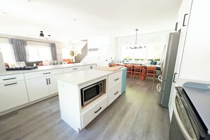A modern kitchen with white cabinetry, a built-in microwave, and a stainless steel refrigerator. - "Upside" New Cottage w Custom Built Bunk Room - Inside LKSD Gates (Lakeside Marblehead)