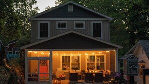 Une maison à deux étages avec un porche et des guirlandes lumineuses.
