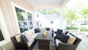 Un espace extérieur aménagé, abrité et doté de mobilier en osier, avec une table centrale et une vue sur la maison en arrière-plan.