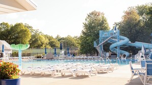 Un espace piscine doté de chaises longues, d’un toboggan et d’une grande structure aquatique bleue.
