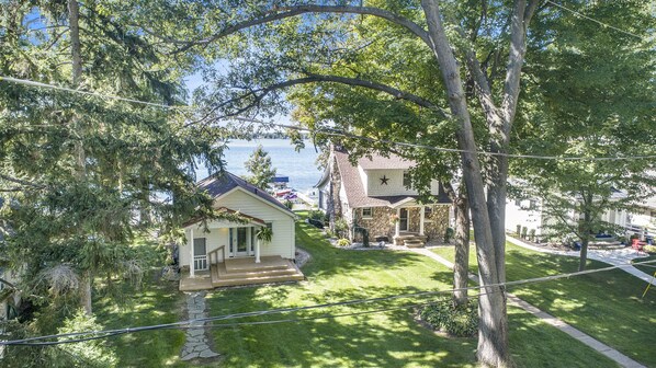 Un quartier résidentiel avec une maison en pierre et une maison blanche ornée d’une étoile sur le mur, le tout entouré d’arbres et offrant une vue sur l’eau.