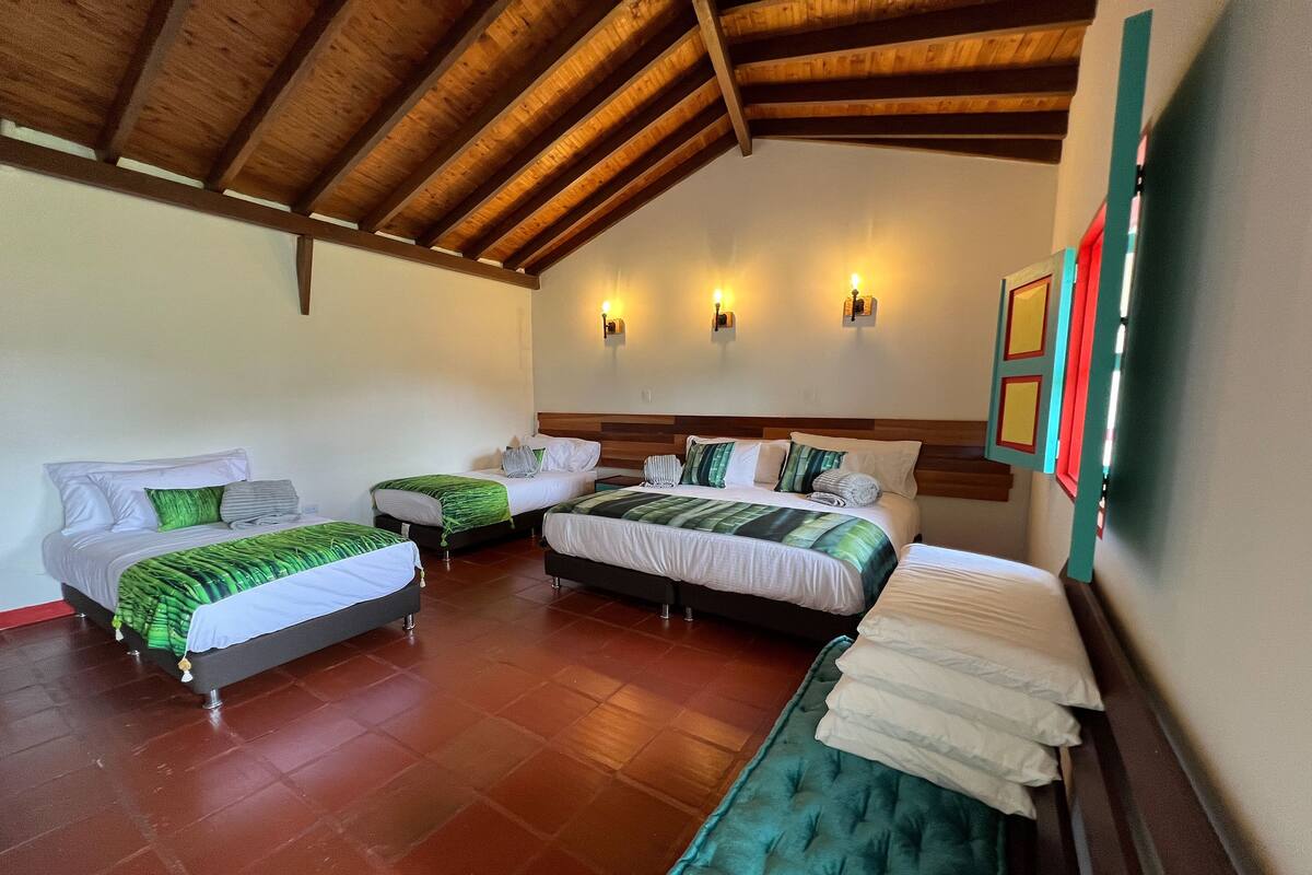 A hotel room with two beds, wooden ceiling beams, wall-mounted lights, and a tiled floor.