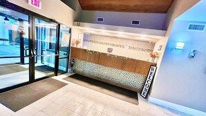 A reception area with a tiled floor, a bench, a reception desk, and an exit sign. - Bayou Inn & Suites (Bayou La Batre)