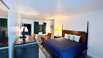 Una habitación de hotel con cama, escritorio, silla, lámpara y mesita de noche.
