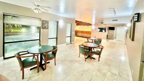 A spacious indoor area with a dining table and chairs, ceiling fans, and large windows with blinds. - Bayou Inn & Suites (Bayou La Batre)
