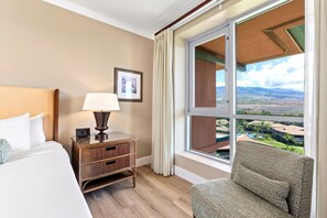 Ein Hotelzimmer mit Bett, Nachttisch mit Lampe, Stuhl, Fenster mit Landschaftsblick und einem gerahmten Bild an der Wand.