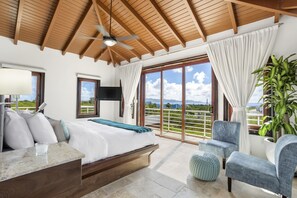 A bedroom with a bed, a desk, a chair, and a large window with a view of the outdoors.