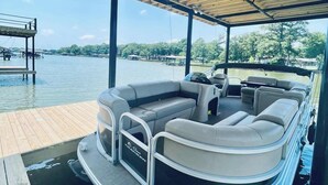 A covered pontoon boat with a seating area, a steering wheel, and a canopy overhead.